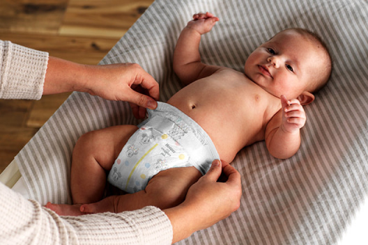 A parent puts a Huggies Little Snugglers Plus Diaper on their baby laying on a changing table